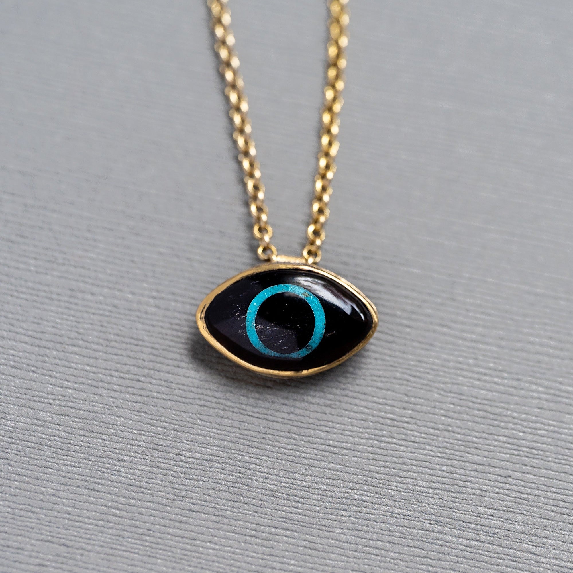 Gold necklace with an obsidian and turquoise eye-shaped pendant on a textured surface