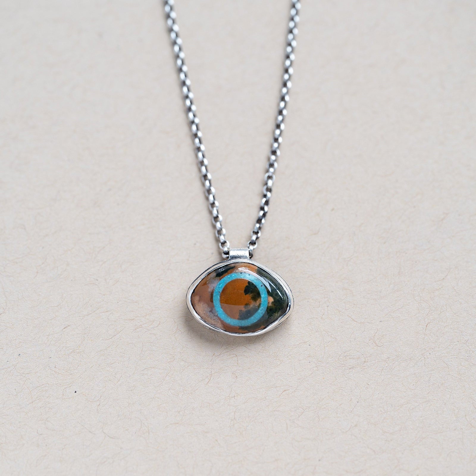 Necklace with a pendant featuring an ocean jasper eye shaped stone on a beige background