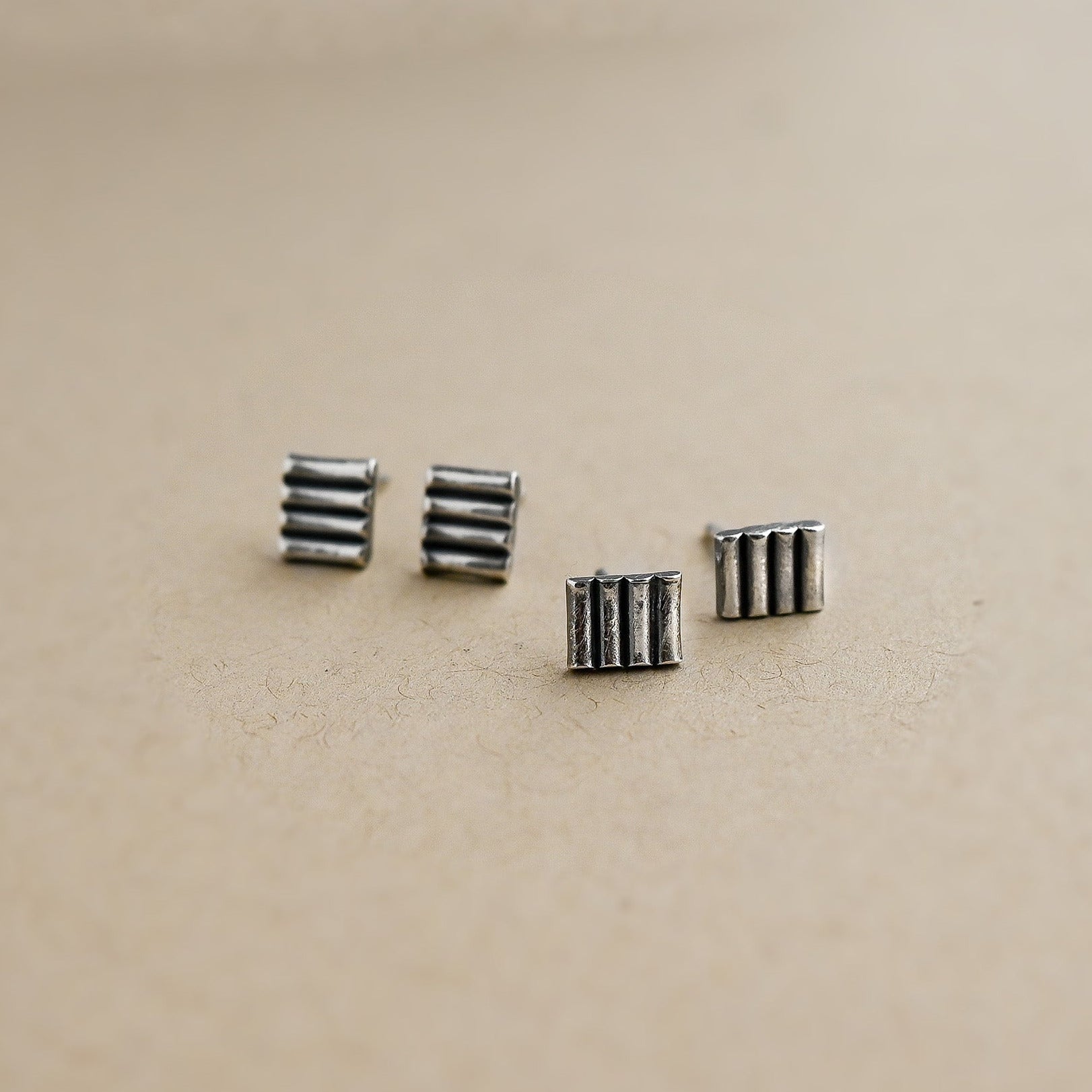 Four small silver earrings on a beige background
