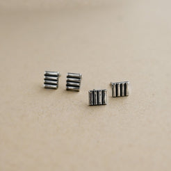 Four small silver earrings on a beige background