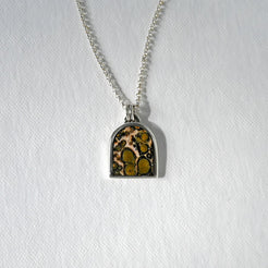 A silver chain necklace with an arched pendant featuring a brown and gold mottled pattern, displayed on a textured white background.