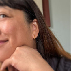 A close-up lifestyle shot of a woman with dark hair resting her chin on her hand, wearing a small gold hoop earring.