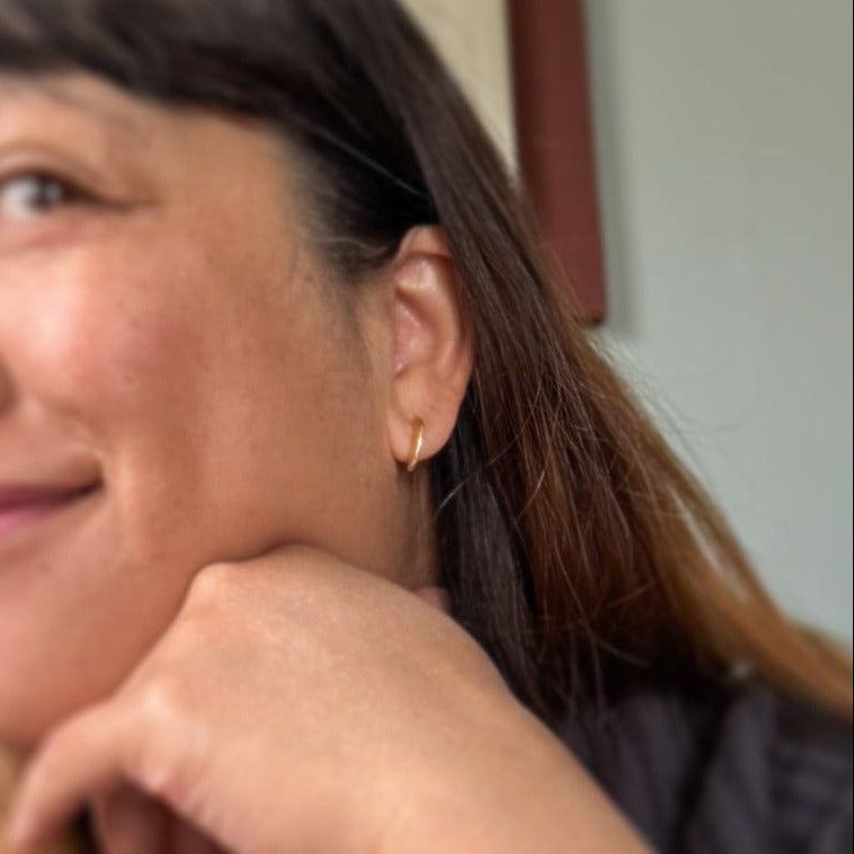 A close-up lifestyle shot of a woman with dark hair resting her chin on her hand, wearing a small gold hoop earring.