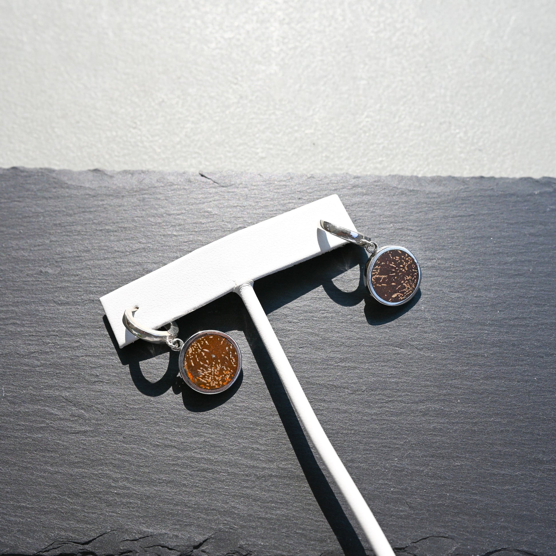 Pair of silver huggie hoop earrings with orange sunburst jasper charms on a slate background