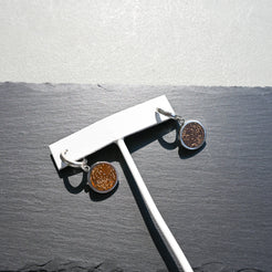 Pair of silver huggie hoop earrings with orange sunburst jasper charms on a slate background