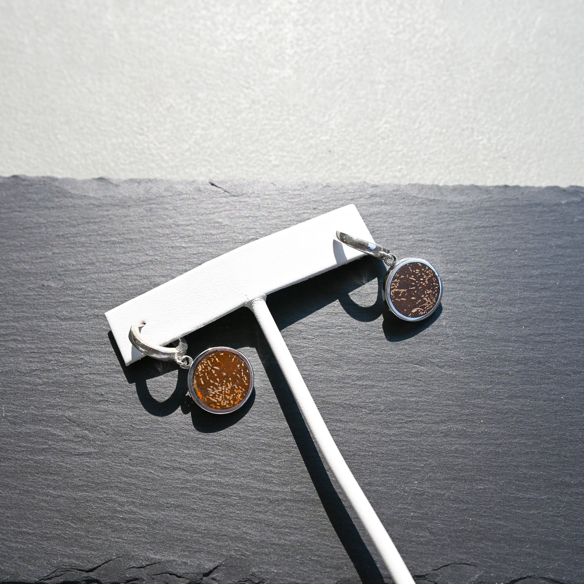 Pair of silver huggie hoop earrings with orange sunburst jasper charms on a slate background