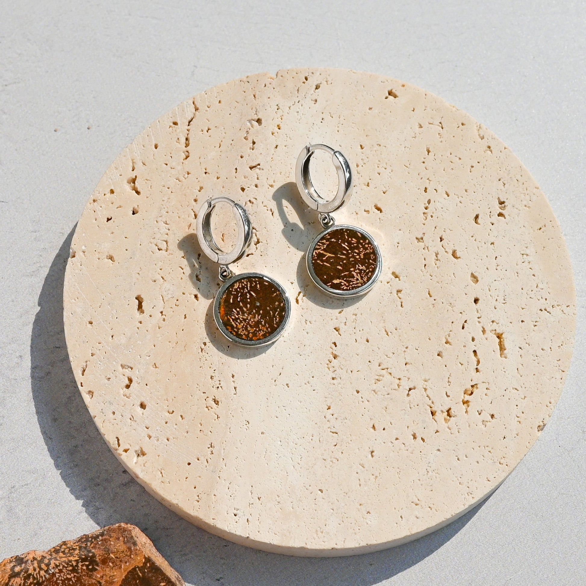Pair of amber stone earrings on a round beige stone surface with a textured gray background.