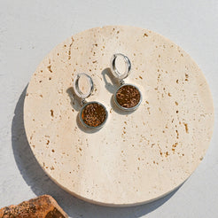 Pair of amber stone earrings on a round beige stone surface with a textured gray background.