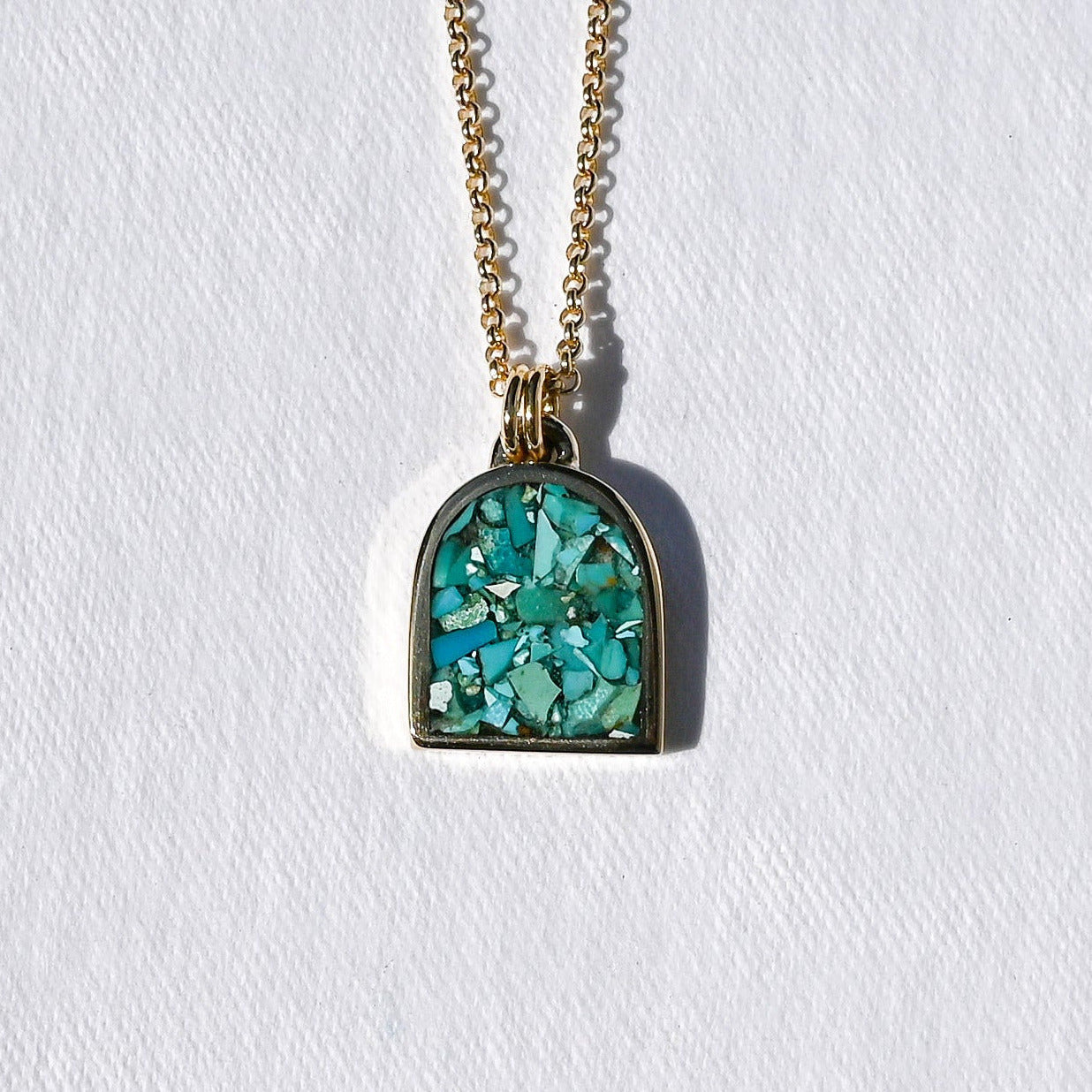 A gold chain necklace with an arched pendant featuring a textured turquoise blue and green stone inlay, set against a plain white background.