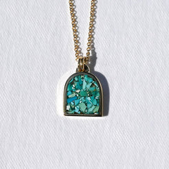 A gold chain necklace with an arched pendant featuring a textured turquoise blue and green stone inlay, set against a plain white background.