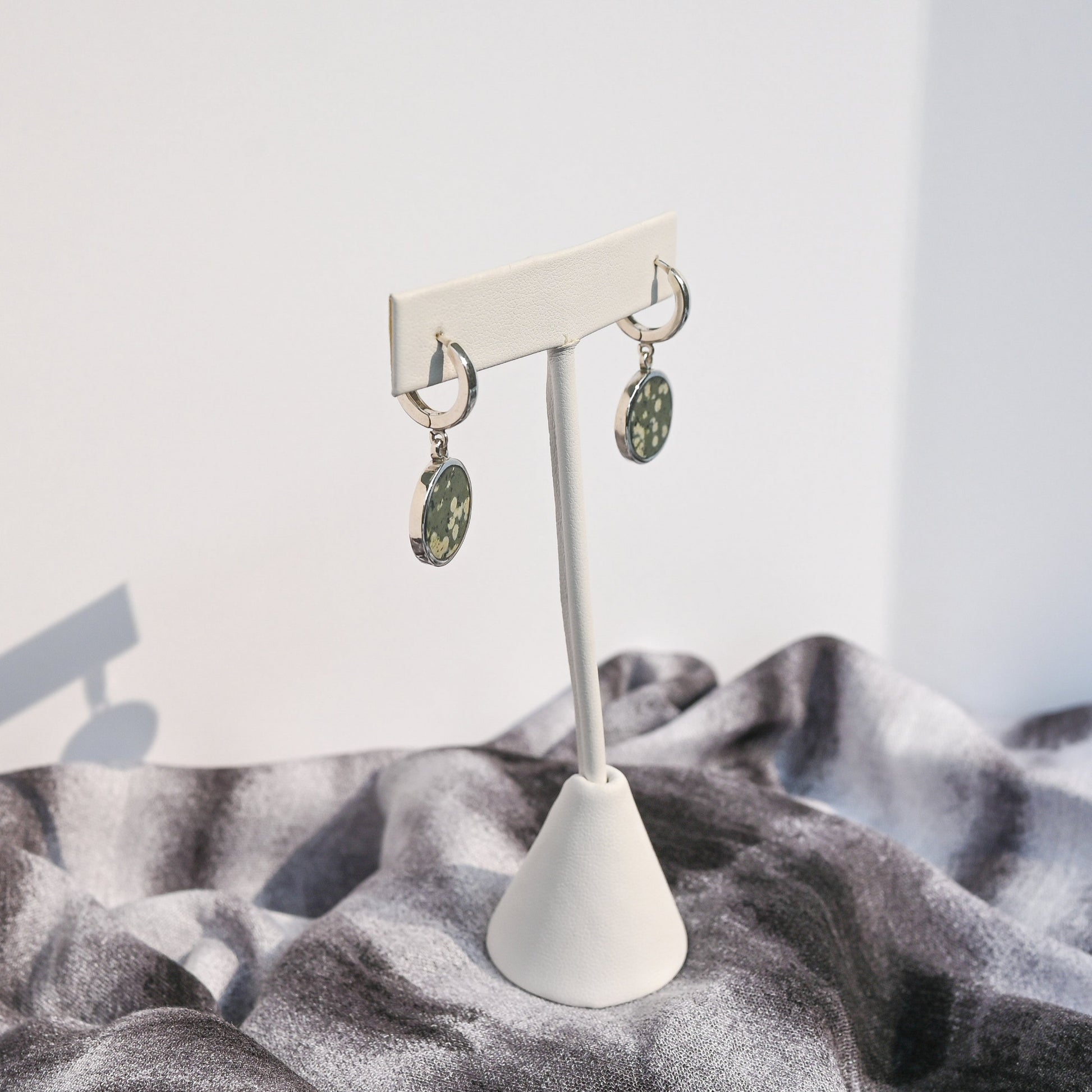 Pair of sterling silver huggie earrings with green variolite stone charms hanging from a white earring form