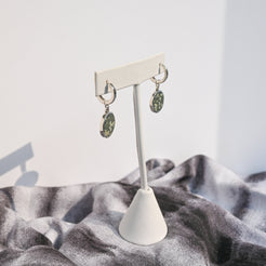Pair of sterling silver huggie earrings with green variolite stone charms hanging from a white earring form