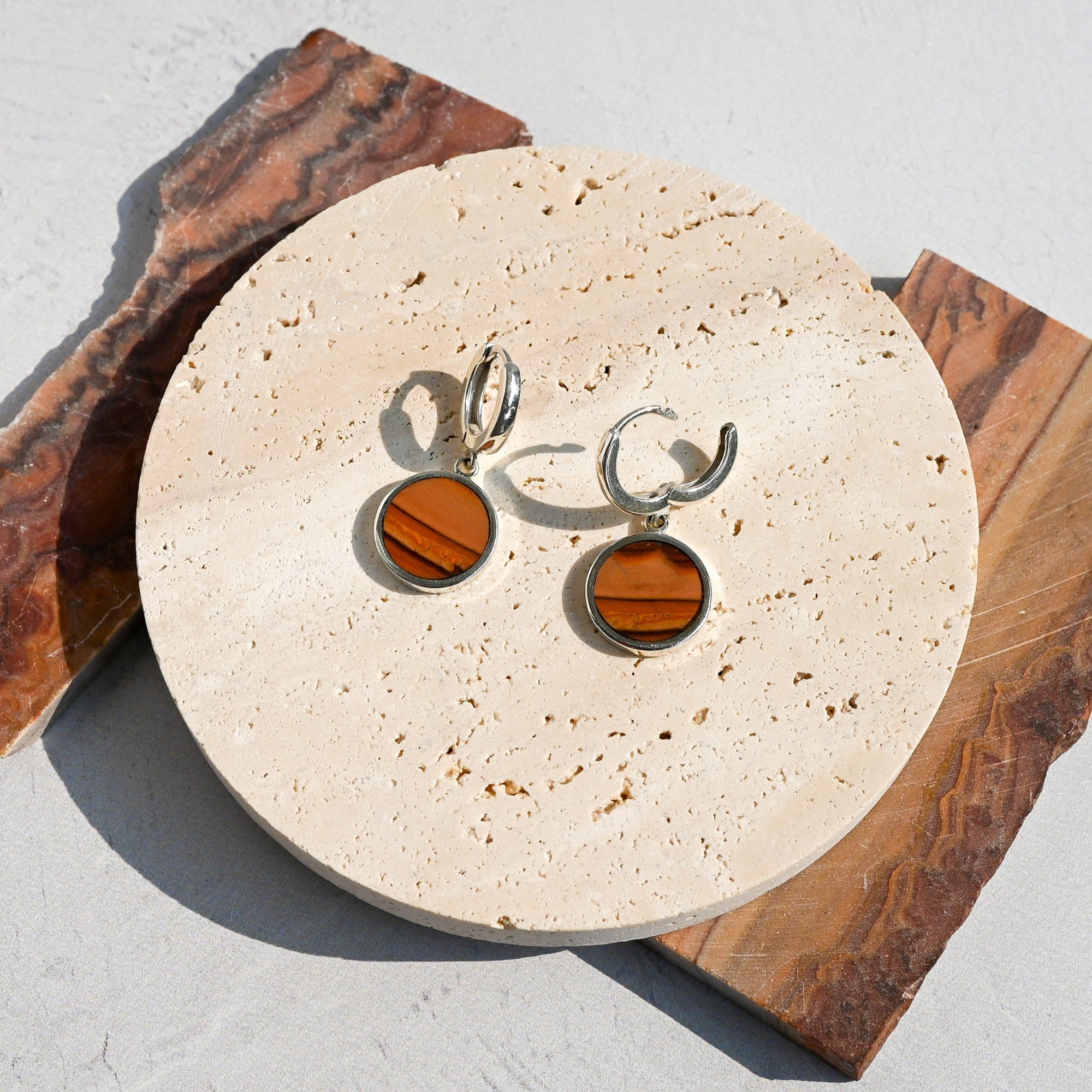 Pair of huggie hoop earrings with dune-like stone pattern on a round stone surface. One hoop is open.