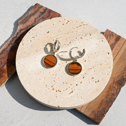 Pair of huggie hoop earrings with dune-like stone pattern on a round stone surface. One hoop is open.