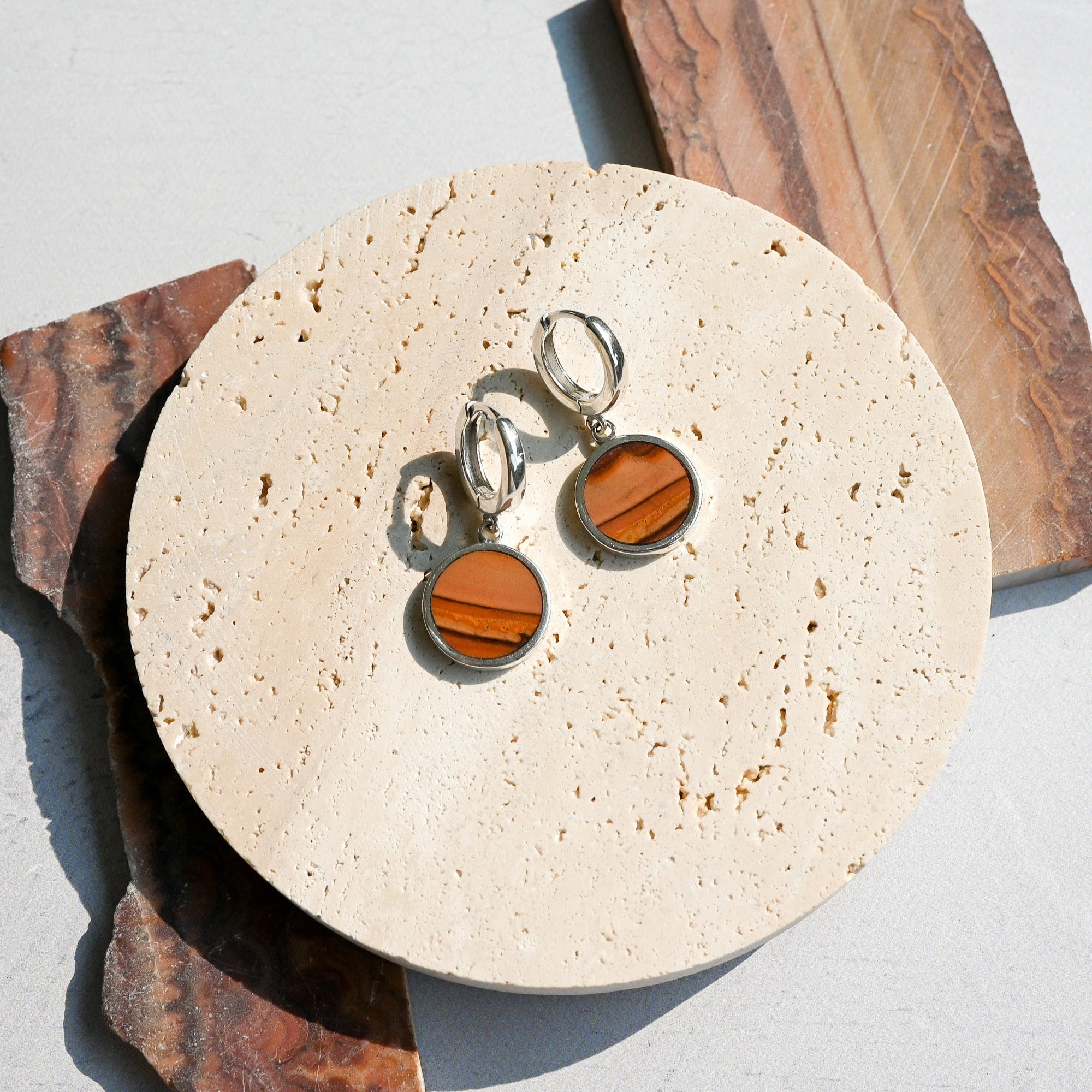Pair of huggie hoop earrings with dune-like stone pattern on a round stone surface.