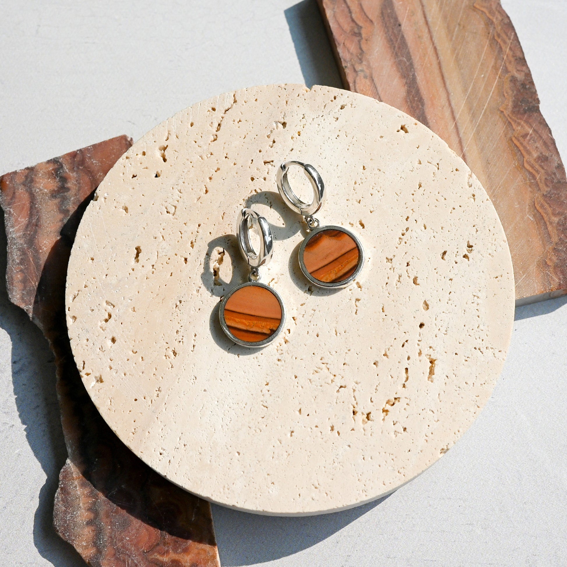 Pair of huggie hoop earrings with dune-like stone pattern on a round stone surface.