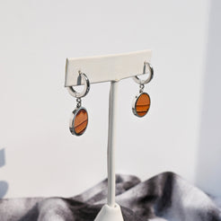 Pair of huggie hoop earrings with dune-like stone pattern hanging from white earring form.