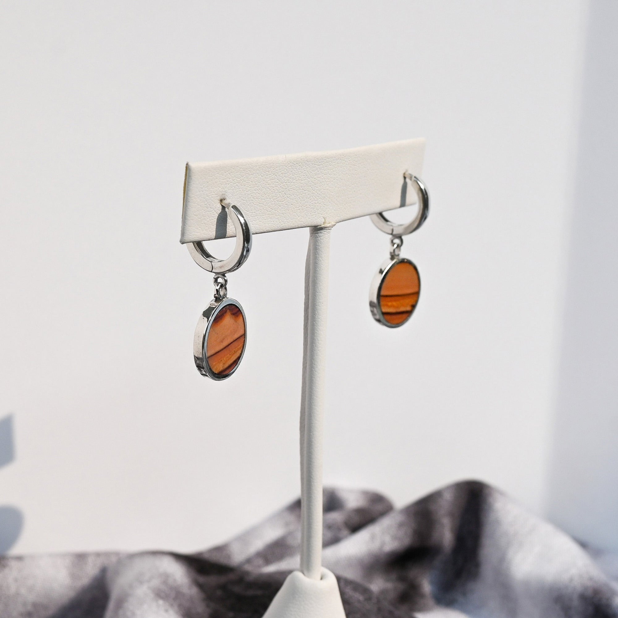 Pair of huggie hoop earrings with dune-like stone pattern hanging from white earring form.