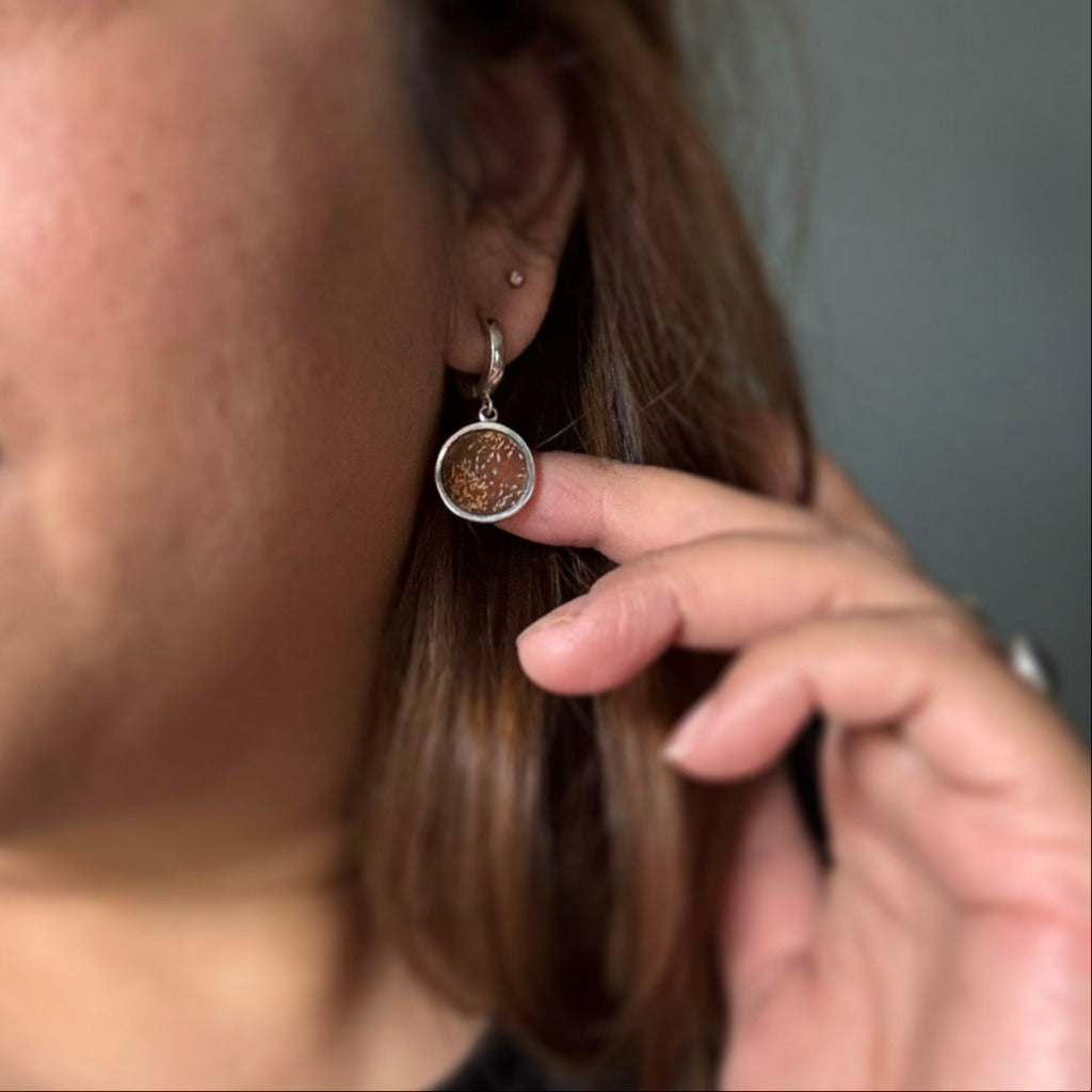 Person wearing silver huggie hoop earring with orange sunburst jasper charms