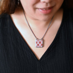 Person wearing a necklace with a checkered pendant against a black background