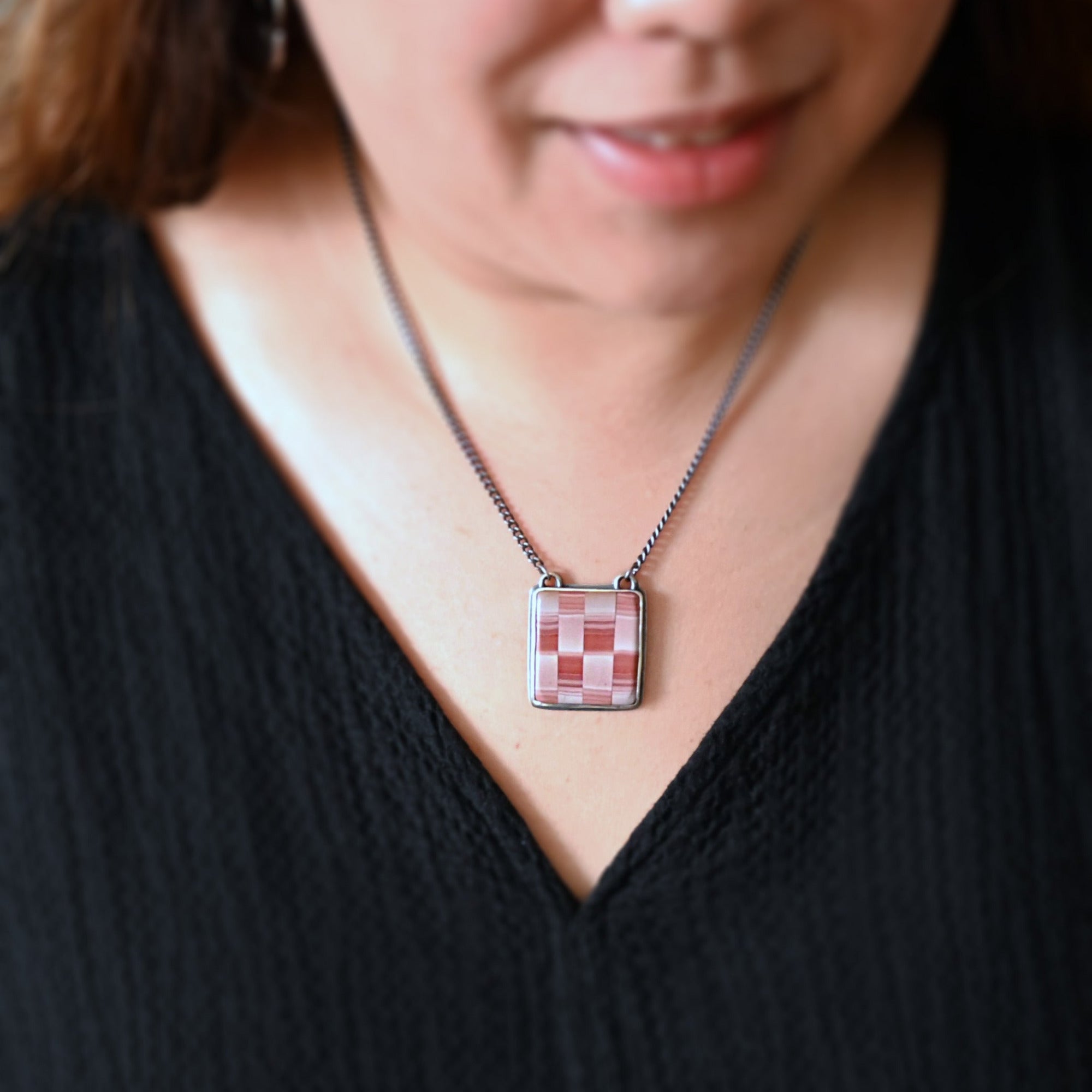 Person wearing a necklace with a checkered pendant against a black background