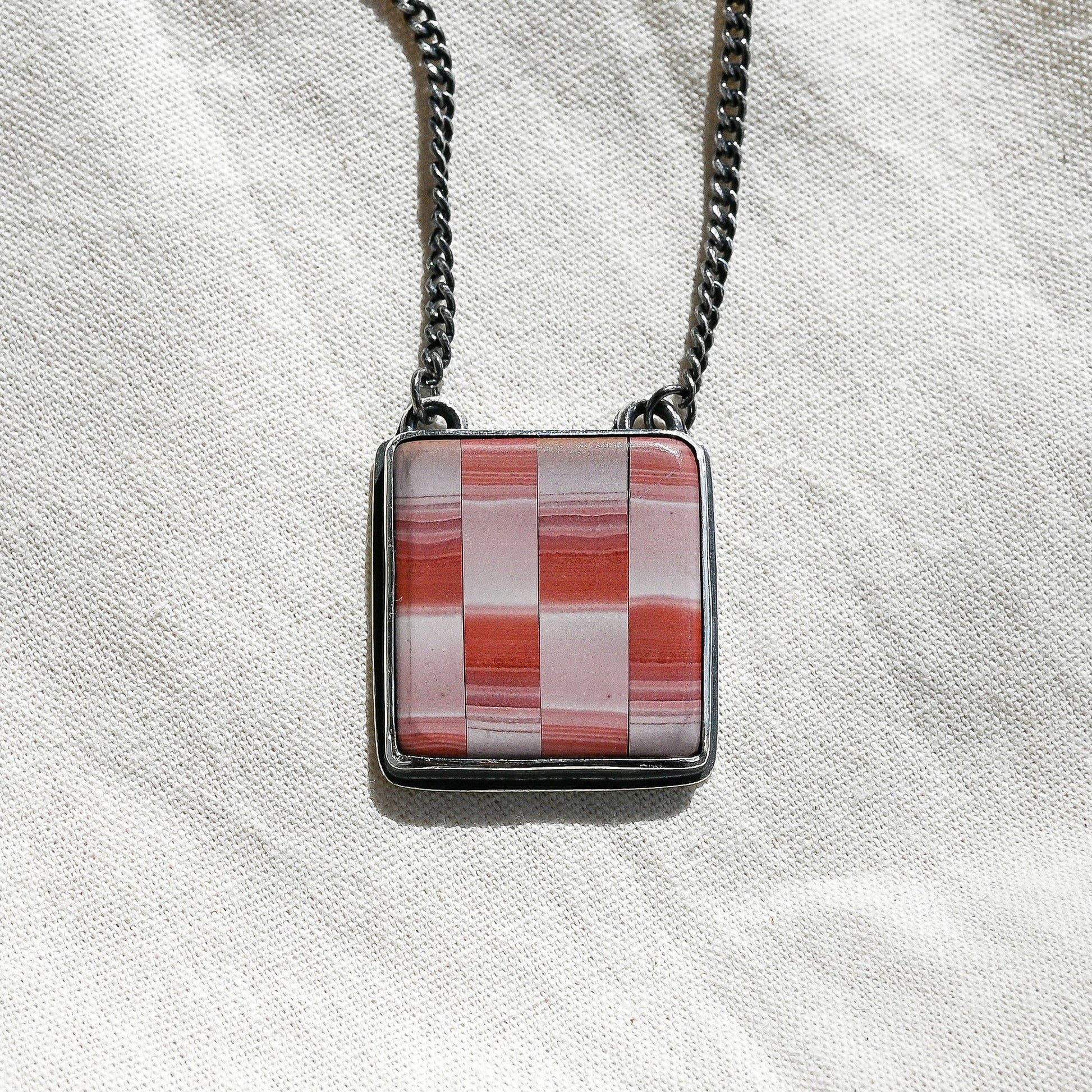Necklace with a square pendant featuring a red and white checkered pattern on a light fabric background.
