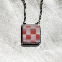 Necklace with a square pendant featuring a red and white checkered pattern on a light fabric background.