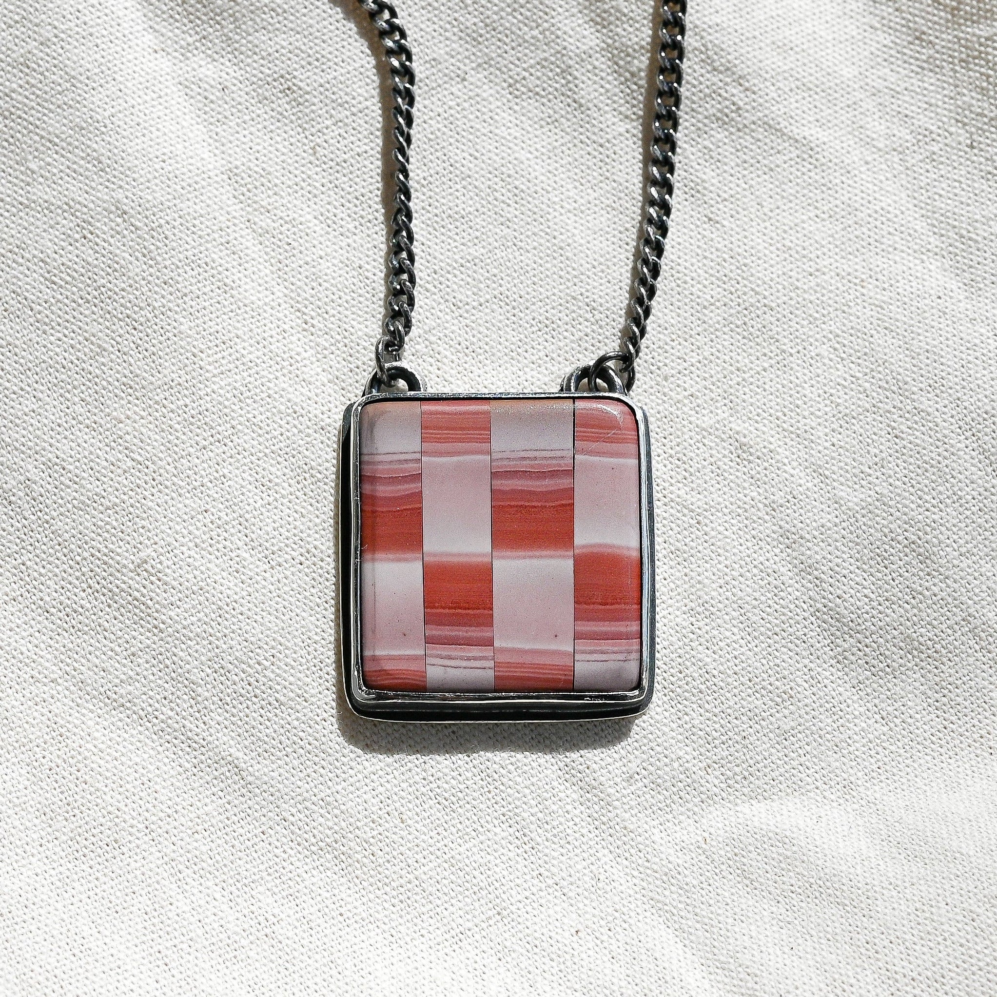 Necklace with a square pendant featuring a red and white checkered pattern on a light fabric background.
