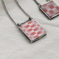 Necklace with a pink and white checkered pendant on a light fabric background