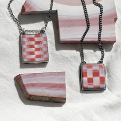 Two necklaces with square pendants featuring a red and white checkered pattern on a textured surface.