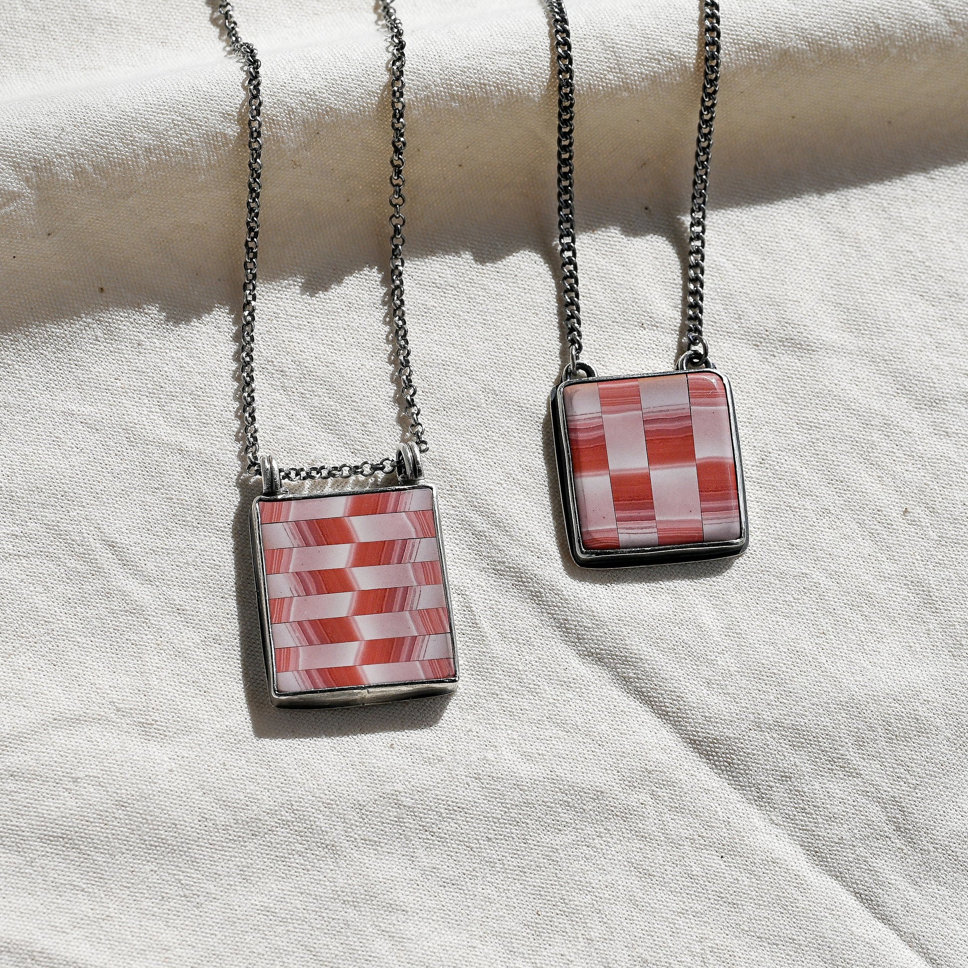 Two necklaces with square pendants on a white fabric background