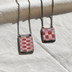 Two necklaces with square pendants on a white fabric background