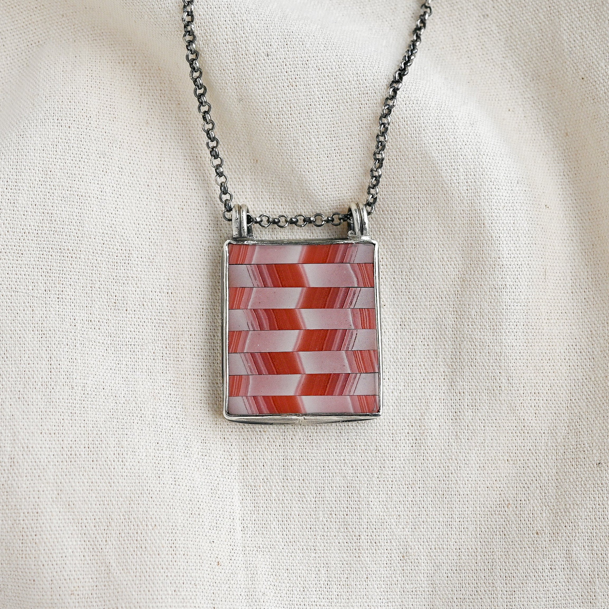 Necklace with a red and white checkered pendant on a beige fabric background
