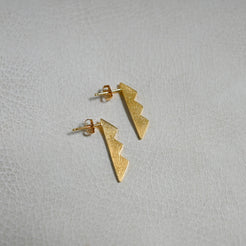A pair of small gold lightning-bolt stud earrings on a light textured surface.