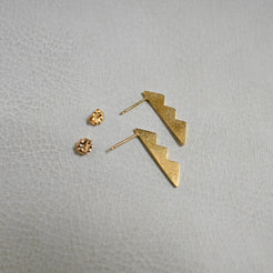 A pair of gold lightning bolt drop earrings with matching textured gold stud earrings, displayed on a light gray textured surface.