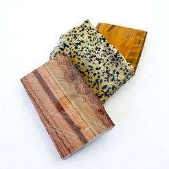 Three rectangular stone or wood blocks with distinct textures and colors, including a speckled beige and black stone, a reddish-brown wood grain, and a golden-brown wood grain, arranged on a plain white background.